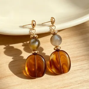 Close up of retro amber acrylic and grey bead dangle earrings with gold metal accents.
