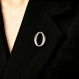 Close-up detail of a minimalist metal oval brooch pin fastened on a black suit lapel.