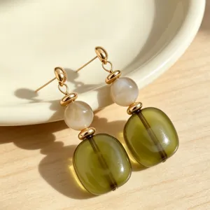 Close-up detail of retro olive green acrylic dangle earrings with gold studs and marbled beads.