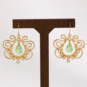 Close-up of vintage gold hollow filigree earrings featuring a green teardrop crystal drop.