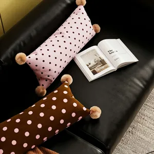 Vue détaillée du long coussin cylindrique à pois avec pompons duveteux sur le canapé.