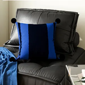 Detail view of modern blue and black striped throw pillow with fluffy pom poms on sofa.