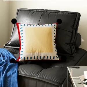 Decorative square throw pillow with black pom poms and colorful geometric border for sofa decor.