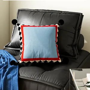 Modern decorative throw pillow featuring black pom poms and a colorful geometric border.