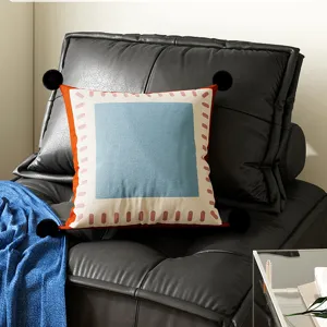Detail shot of decorative throw pillow with black pom-poms, blue square and pink dash border.