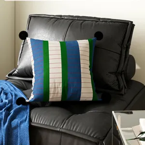 Close-up detail of colorful striped throw pillow with black pom-poms on modern leather sofa.