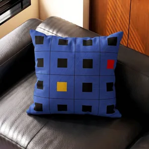 Detalle de cojín geométrico azul con patrón de cuadrícula negra y cuadrados de colores en el sofá.