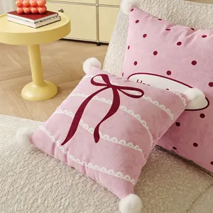 Pink bow throw pillow detail with cute white plush balls for cozy living room sofa decor.