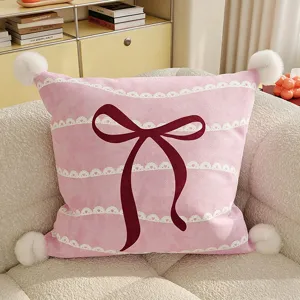 Detail view of pink bow cushion, soft plush fabric with cute pom poms and lace trim
