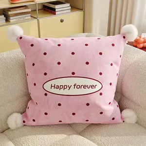 Close-up detail of cute pink polka dot cushion with white pom poms on cozy sofa decor.
