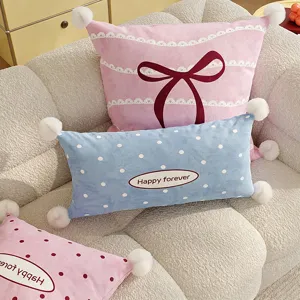 Close-up detail of cute decorative throw pillow with bow and pom poms on cozy sofa setup.