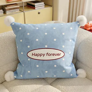 Detailed view of soft blue polka dot cushion with pom-poms and embroidered text for cozy sofa decor.