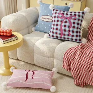Cute decorative throw pillow with bow and pom-poms for cozy living room sofa decor.