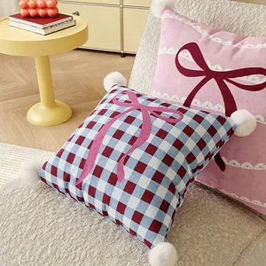 Decorative plush throw pillow with cute bow design and pom poms for living room sofa.