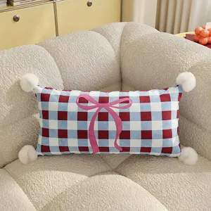 Charming blue and red plaid throw pillow with pink bow and pom-poms for cozy living room decor.