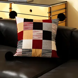 Detailed close-up shot of a geometric patchwork throw cushion with playful black pom-pom corners.