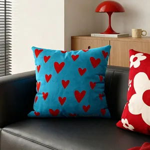 Fodera per cuscino in velluto blu con cuori rossi, presentata su un divano moderno in pelle nera.