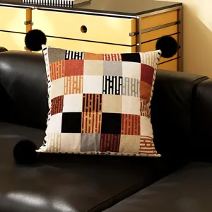 Detailed view of a retro geometric throw pillow with black pom-poms on a modern black leather sofa.