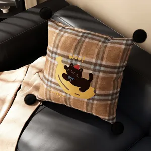 Detail shot of British style plaid throw pillow with cute black cat embroidery and pom poms.