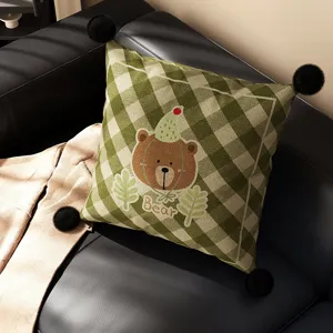 Green plaid throw pillow with cute cartoon bear embroidery, fluffy black pom-poms, soft cushion core.