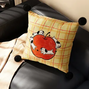 Detail shot of a yellow plaid pillow with cute cartoon dogs and red apple graphic on black sofa.