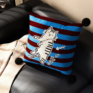 Detail view of striped cushion with cute cat print and pom-poms for cozy home decor.