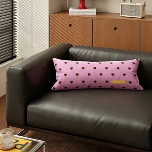 Pink long bolster cushion featuring brown heart pattern, soft velvet fabric sofa detail.
