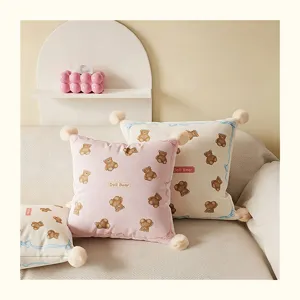 Cozy cream bear pillow detail view, soft plush cushion with cute cartoon print and pom poms.