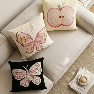 Detail shot of cute butterfly and apple embroidered throw pillows on cozy sofa, aesthetic decor.