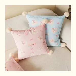 Cute plush throw pillow with pom-poms and rabbit cartoon print for cozy sofa decor.