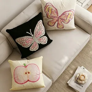 Detail view of Korean style embroidered butterfly and apple throw pillows on a cozy sofa.