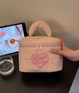 Detail view of the pink quilted cosmetic bag featuring a cute heart embroidery design and handle.