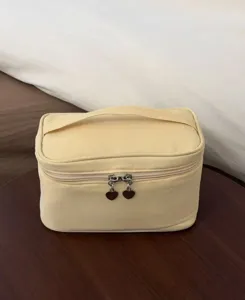 Detail view of the yellow cosmetic bag, featuring a convenient handle and heart zipper pulls.