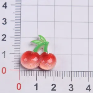 Primer plano de abalorio cereza de resina, fruta roja brillante con hojas para decoración DIY.