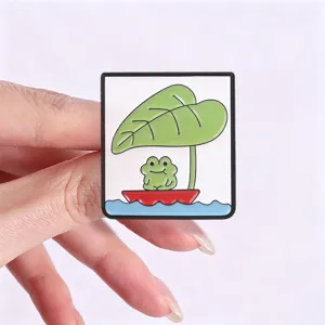 Close-up detail shot of a cute cartoon frog and lotus leaf boat metal enamel brooch pin.