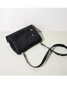 Detalle de bolso bandolera negro de nailon elegante, con diseño de solapa y herrajes metálicos.