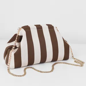 Détail de trousse de maquillage en tricot rayé marron et blanc, texture et chaîne dorée.