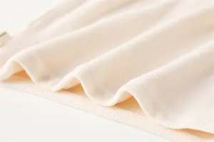 Close-up van de gebreide nekwarmer stof in beige met een zachte en warme textuur.