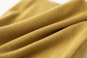 Detailopname van mosterdgele geribbelde gebreide stof met zachte textuur en warme details.