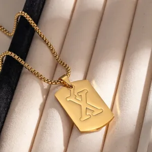 Dettaglio di una collana con ciondolo a targhetta in acciaio dorato con lettera X intagliata.
