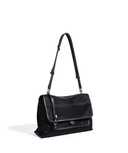 Vista detallada del bolso bandolera negro de nylon con solapa y herrajes metálicos.