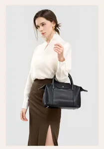 Detailed view of a black genuine leather top-handle bag worn by a model in a studio setting.