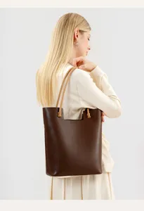 Detailed back view presentation of a brown leather tote bag with tan handles on a model.