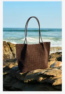 Brown suede woven tote bag detail showing handcrafted leather texture and seaside rocks background.