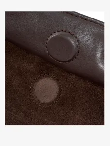 Close-up detail of brown suede leather pillow bag showing fine stitching and magnetic snap closure.