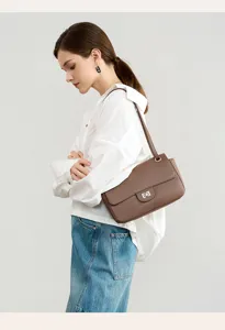 Detail shot of brown leather shoulder bag with metal twist lock, worn by model for style.