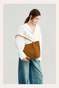 Detailed shot of woman wearing a brown suede woven shoulder bag, showcasing stylish design.