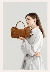 Detail view of a brown suede pillow bag held by a model, showcasing vintage commuter style.
