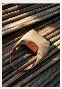 Detailed shot of a stylish beige nylon shoulder bag with brown leather flap on bamboo.