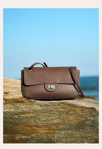 Detail shot of brown leather shoulder bag featuring metal turn-lock closure and outdoor scene.